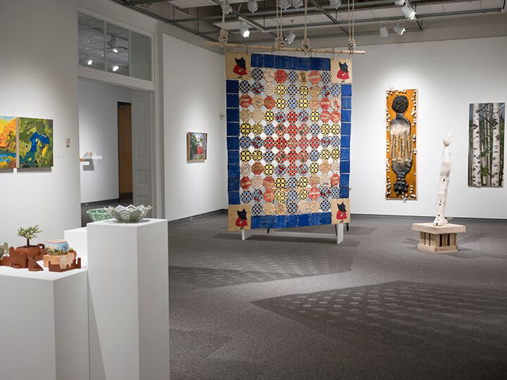 A quilt is hung among the other pieces of art in the gallery.